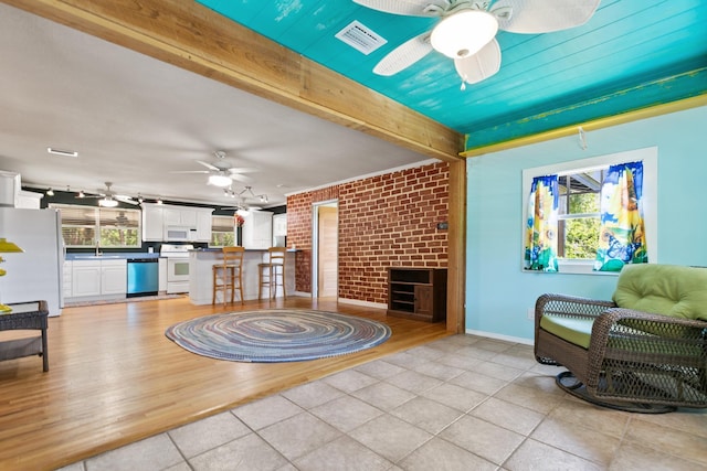living room featuring light tile patterned floors, brick wall, ceiling fan, and a healthy amount of sunlight
