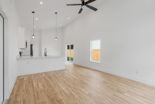 unfurnished living room featuring ceiling fan, light hardwood / wood-style floors, sink, and high vaulted ceiling