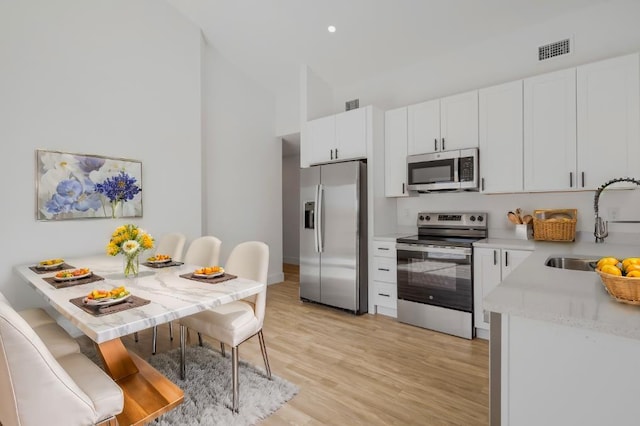 kitchen with appliances with stainless steel finishes, light wood-type flooring, white cabinetry, and sink