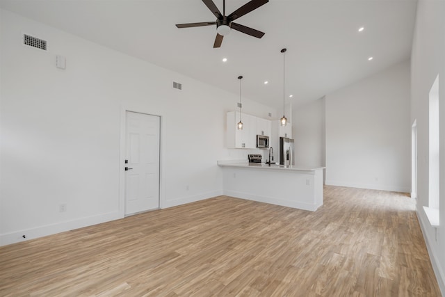 unfurnished living room with a high ceiling, light wood-type flooring, and ceiling fan