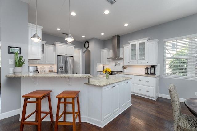 kitchen featuring wall chimney exhaust hood, light stone counters, dark hardwood / wood-style flooring, stainless steel refrigerator with ice dispenser, and white cabinets