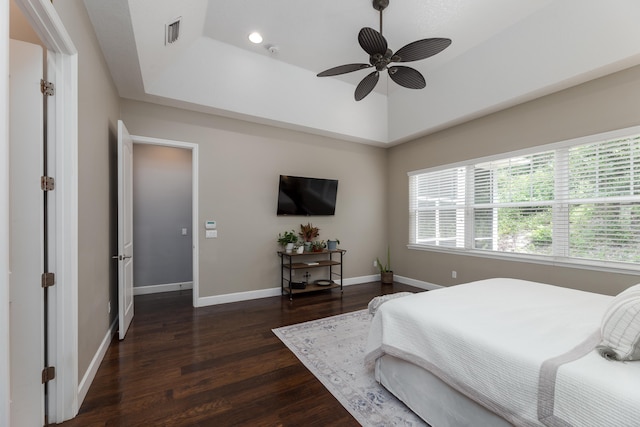 bedroom with dark hardwood / wood-style flooring, a tray ceiling, multiple windows, and ceiling fan