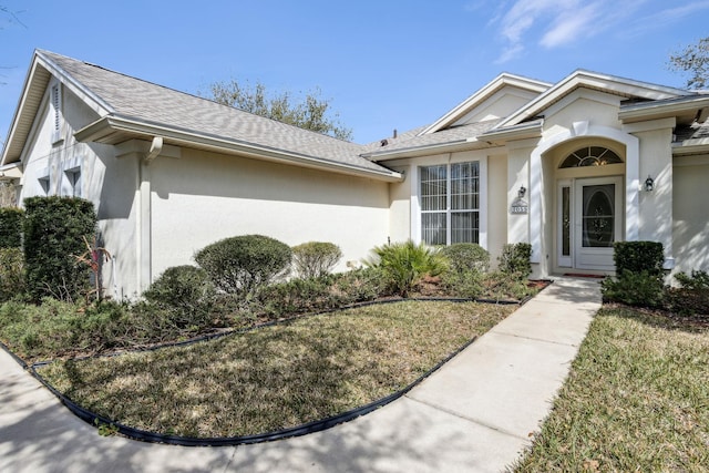 view of front facade with a shingled roof and stucco siding