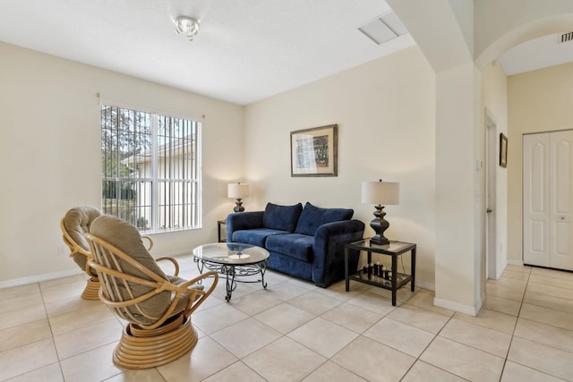 living room featuring light tile patterned floors, arched walkways, visible vents, and baseboards