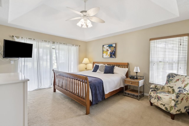 bedroom featuring multiple windows, a raised ceiling, and light colored carpet