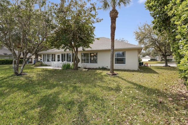 back of house featuring stucco siding, a sunroom, and a yard