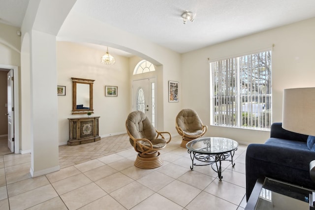 living area with arched walkways, light tile patterned flooring, a textured ceiling, and baseboards