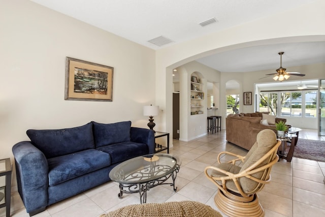 living room featuring arched walkways, built in shelves, light tile patterned floors, and visible vents