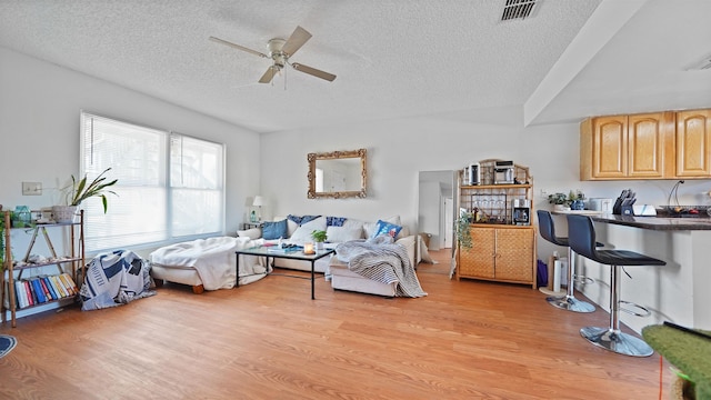 living room with ceiling fan, a textured ceiling, and light hardwood / wood-style floors