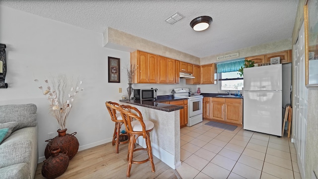 kitchen featuring kitchen peninsula, white appliances, light tile patterned flooring, a textured ceiling, and sink