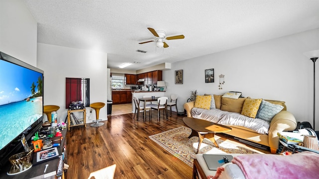 living room with a textured ceiling, ceiling fan, and dark wood-type flooring