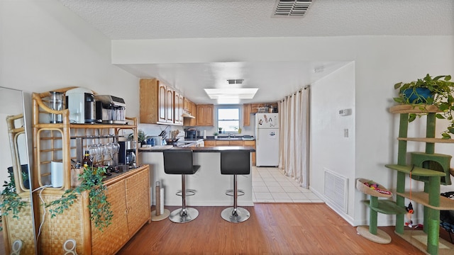 kitchen featuring a textured ceiling, white fridge, light hardwood / wood-style floors, a kitchen breakfast bar, and kitchen peninsula