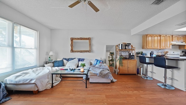 living room with light wood-type flooring, ceiling fan, and a textured ceiling