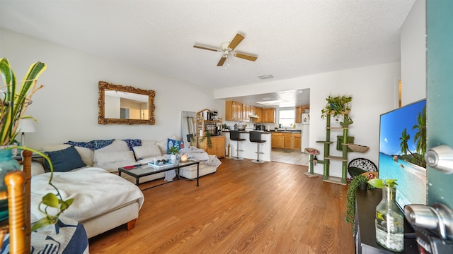 living room with ceiling fan, a textured ceiling, and light hardwood / wood-style flooring