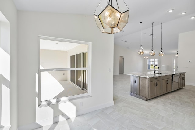 kitchen featuring light stone counters, a kitchen island with sink, sink, dishwasher, and hanging light fixtures