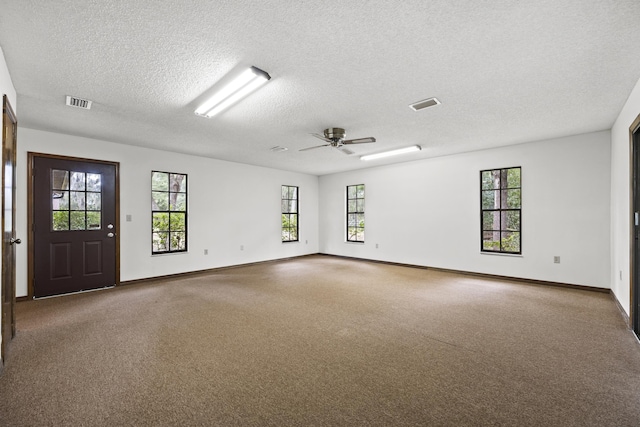 empty room with a wealth of natural light, ceiling fan, and a textured ceiling