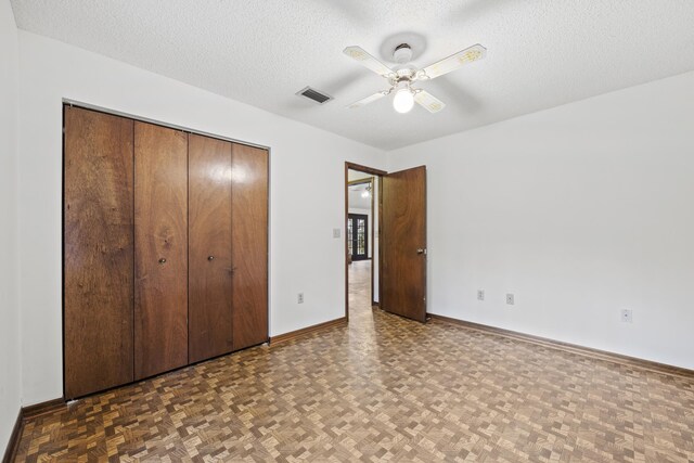 unfurnished bedroom with a textured ceiling, a closet, ceiling fan, and dark parquet floors