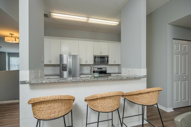 kitchen with white cabinets, a breakfast bar, kitchen peninsula, and appliances with stainless steel finishes