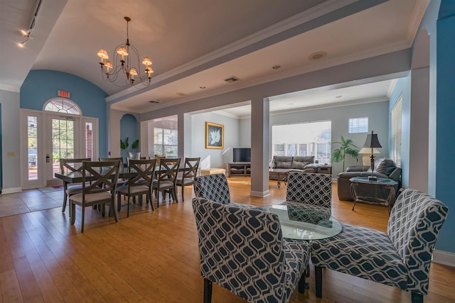 dining area with a chandelier, hardwood / wood-style floors, vaulted ceiling, and crown molding