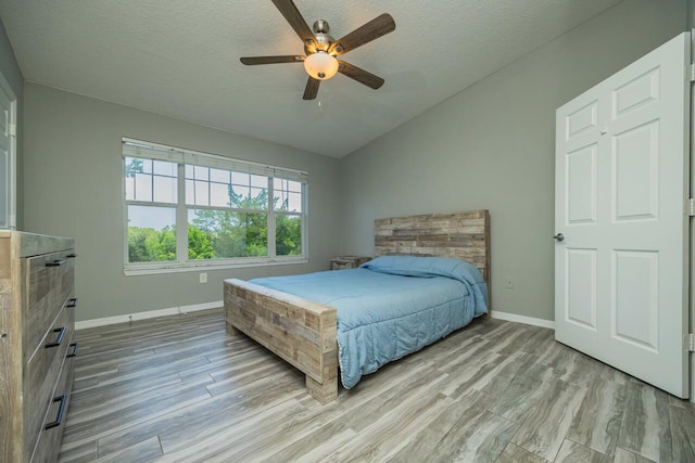 bedroom featuring ceiling fan, wood-type flooring, a textured ceiling, and lofted ceiling