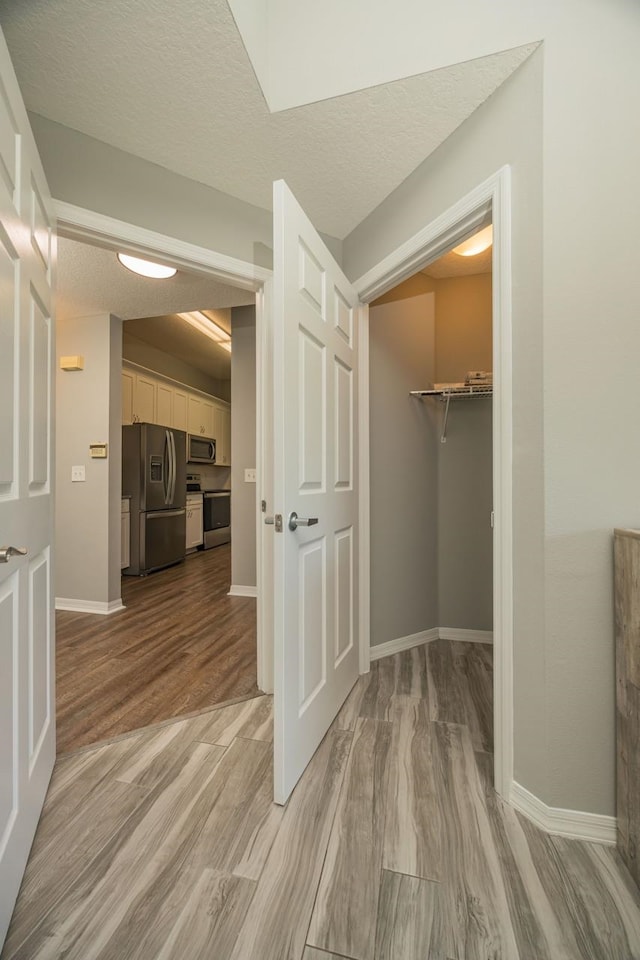 corridor with a textured ceiling and light wood-type flooring