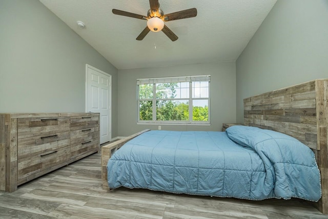 bedroom featuring a textured ceiling, light hardwood / wood-style flooring, vaulted ceiling, and ceiling fan