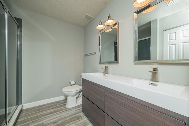 bathroom with wood-type flooring, a textured ceiling, toilet, and a shower with shower door