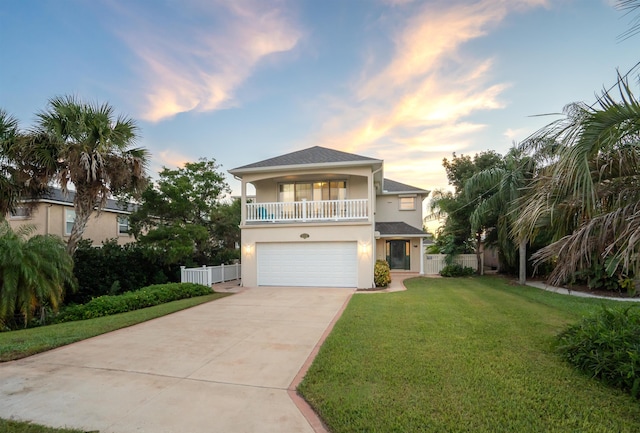 view of front of home featuring concrete driveway, a balcony, fence, a yard, and stucco siding