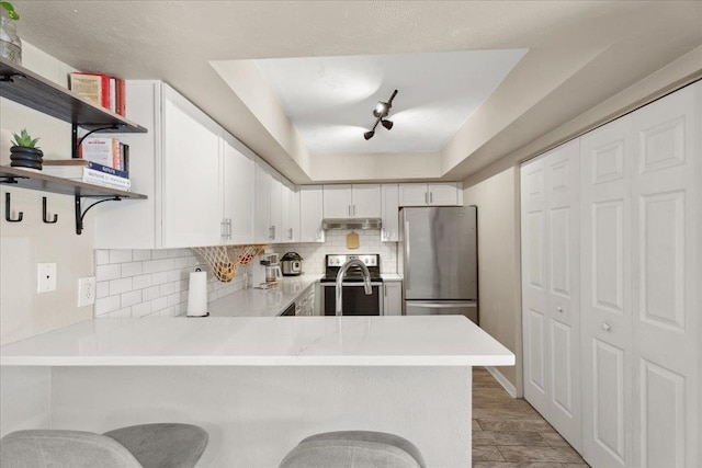 kitchen featuring open shelves, stainless steel appliances, light countertops, backsplash, and a peninsula