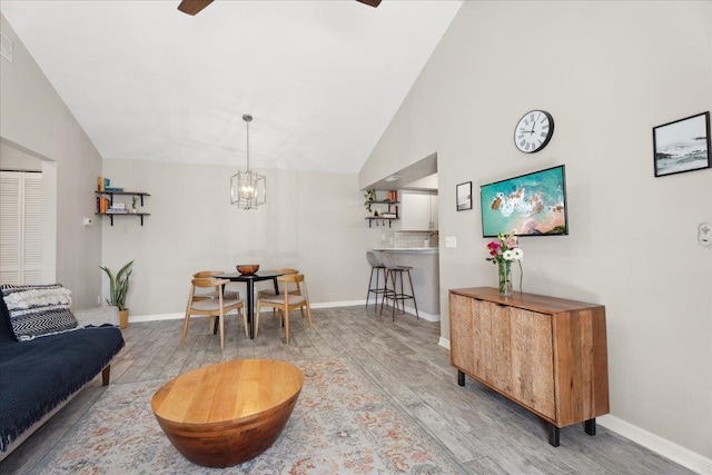 living room featuring high vaulted ceiling, an inviting chandelier, wood finished floors, and baseboards