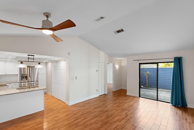 unfurnished living room with sink, ceiling fan, vaulted ceiling, and light hardwood / wood-style flooring