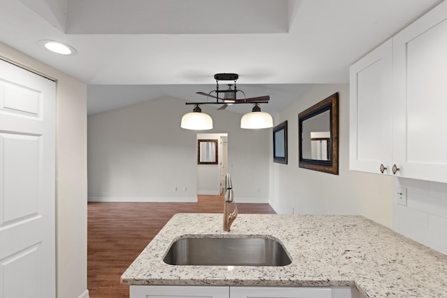 kitchen featuring dark wood-type flooring, light stone counters, sink, white cabinetry, and decorative light fixtures