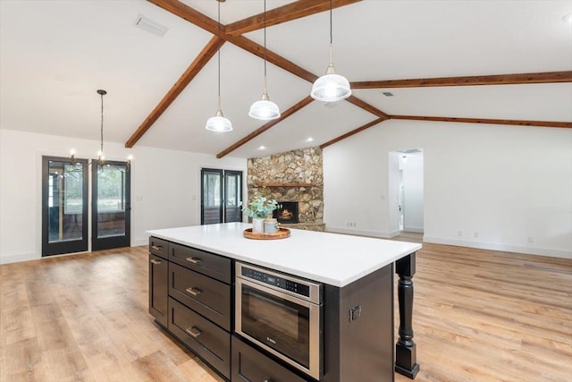 kitchen with light wood-style floors, a stone fireplace, lofted ceiling with beams, and open floor plan