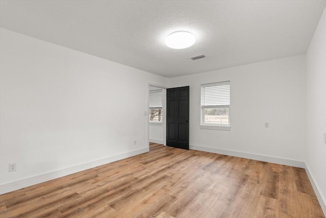 empty room featuring visible vents, baseboards, light wood-style floors, and a textured ceiling