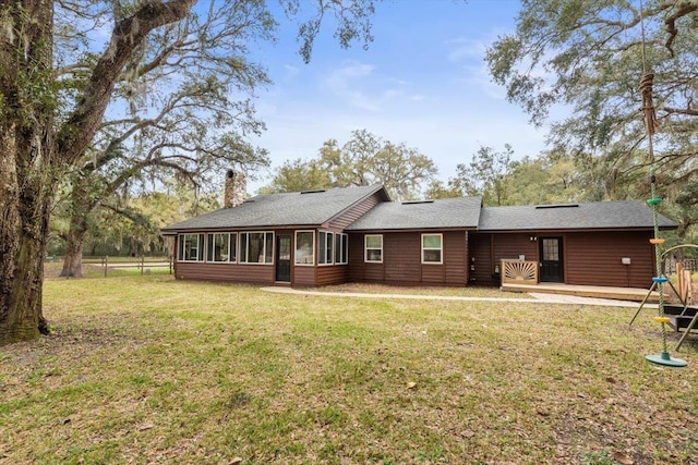 back of property featuring a lawn, a deck, a chimney, and a sunroom