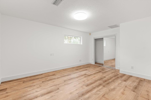 interior space featuring visible vents, light wood-style flooring, a textured ceiling, a closet, and baseboards