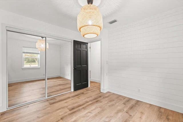 unfurnished bedroom featuring light wood-type flooring, visible vents, baseboards, and a closet