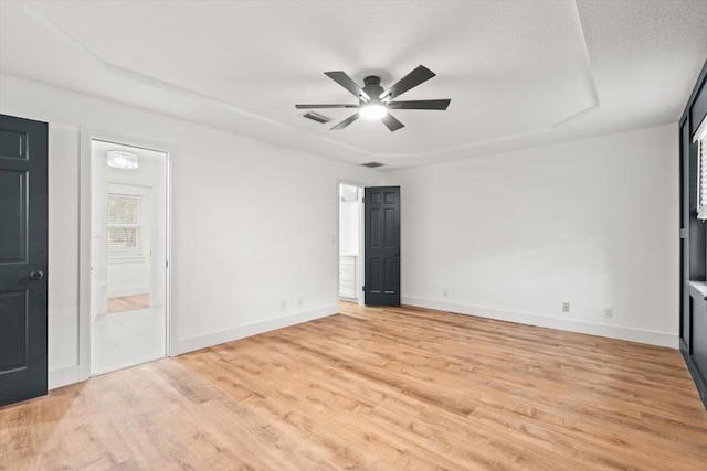 unfurnished bedroom with a textured ceiling, baseboards, ensuite bathroom, and light wood-style floors