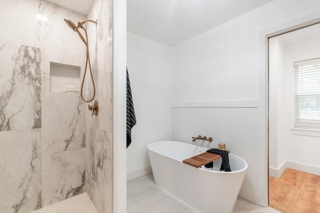 full bath featuring a soaking tub, baseboards, and a marble finish shower