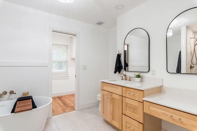 full bath with vanity, a wainscoted wall, visible vents, a freestanding tub, and toilet