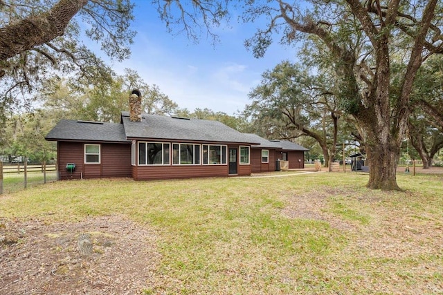 back of house featuring fence, a yard, roof with shingles, a sunroom, and a chimney