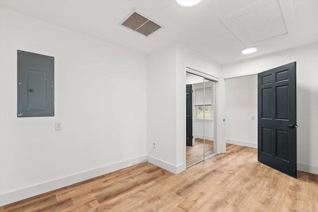 unfurnished room with visible vents, electric panel, light wood-style floors, baseboards, and attic access