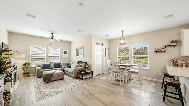 living room featuring a textured ceiling, light hardwood / wood-style floors, and ceiling fan with notable chandelier