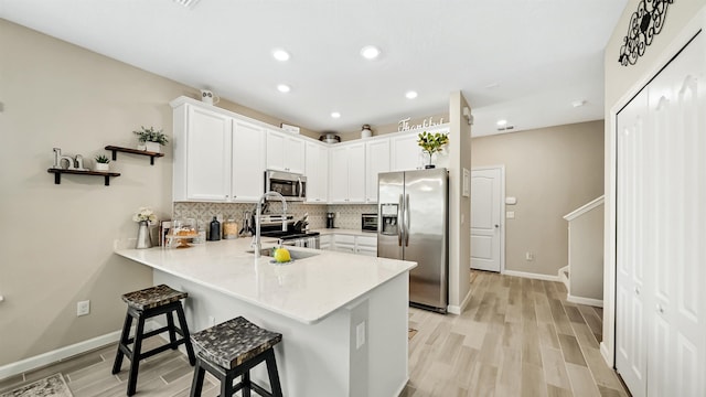 kitchen with white cabinets, sink, light wood-type flooring, appliances with stainless steel finishes, and a kitchen bar