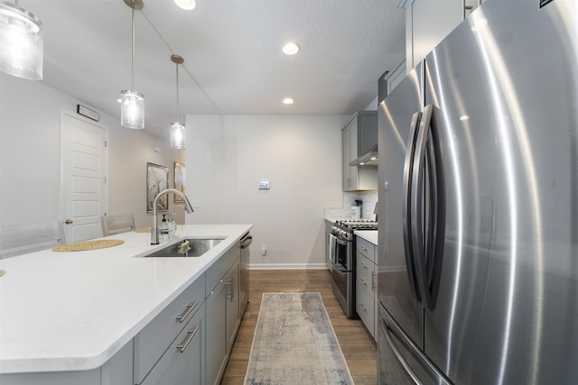 kitchen featuring sink, hanging light fixtures, gray cabinets, an island with sink, and stainless steel appliances