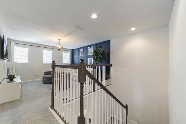 corridor with carpet floors, a notable chandelier, and a textured ceiling