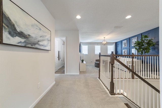 hall with an inviting chandelier, light carpet, and a textured ceiling