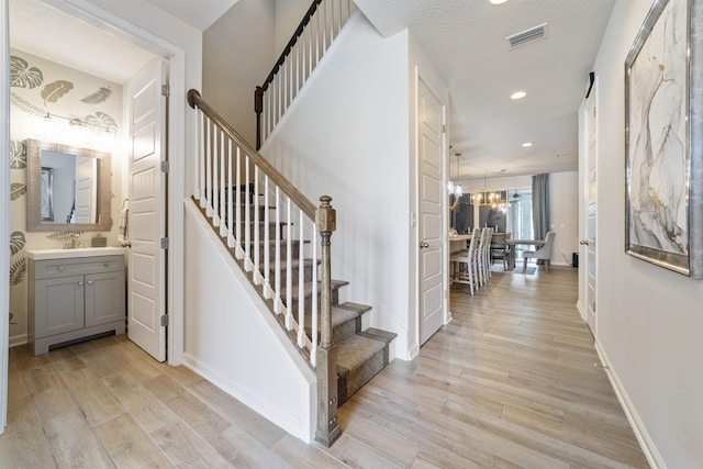 stairway with an inviting chandelier, sink, and hardwood / wood-style floors