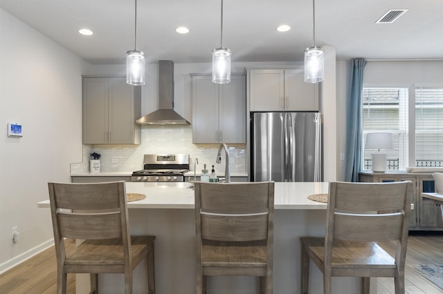 kitchen with pendant lighting, appliances with stainless steel finishes, gray cabinets, and wall chimney range hood