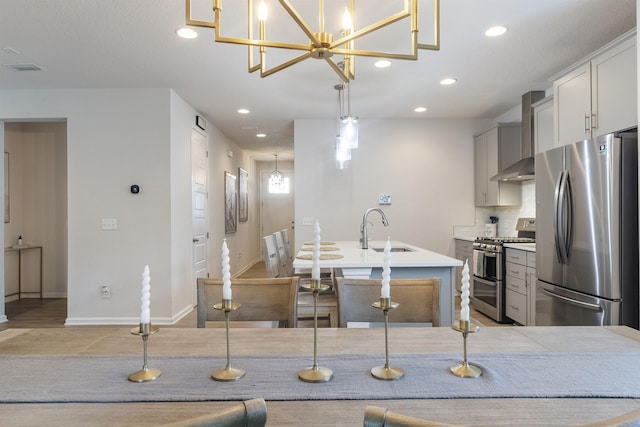 kitchen with pendant lighting, sink, wall chimney exhaust hood, and appliances with stainless steel finishes